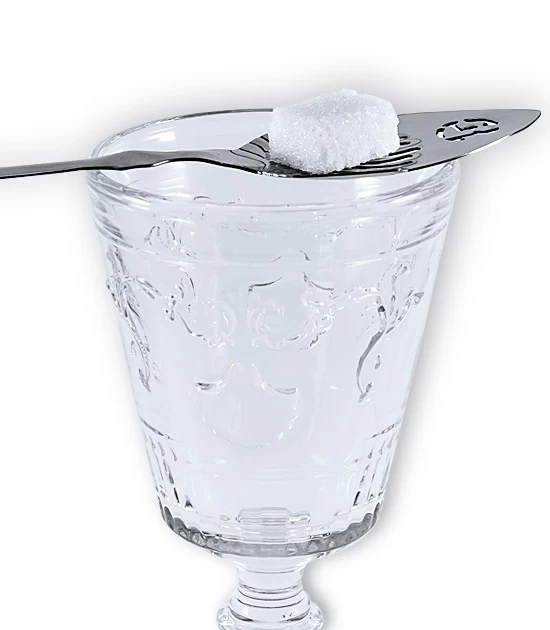 Detailed image of absinthe spoon on the rim of the glass with a cube of sugar set on top.